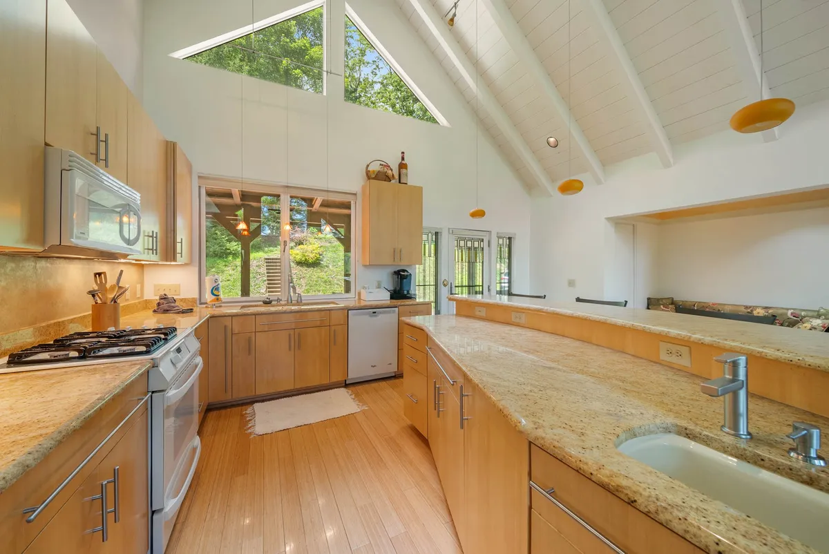 A spacious kitchen with granite countertops, large windows framing lush outdoor views, and a vaulted ceiling that fills the space with natural light. Modern appliances and an inviting layout suggest a perfect setting for cooking, entertaining, and gathering with loved ones.