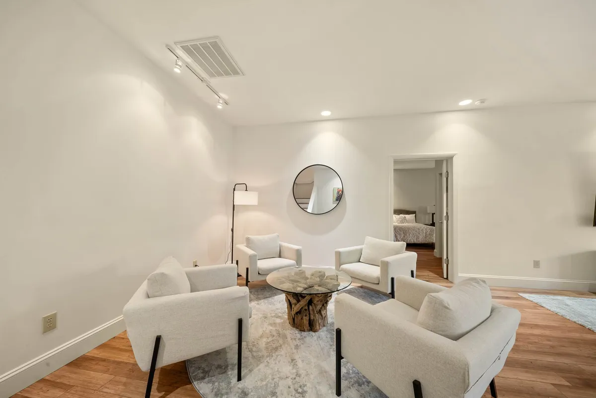 This image features a welcoming seating arrangement centered around a round coffee table, with comfortable chairs and a floor lamp, set against a backdrop that includes a mirror reflecting natural light. The space suggests a place for guests to gather, share stories, and plan their next local adventure.