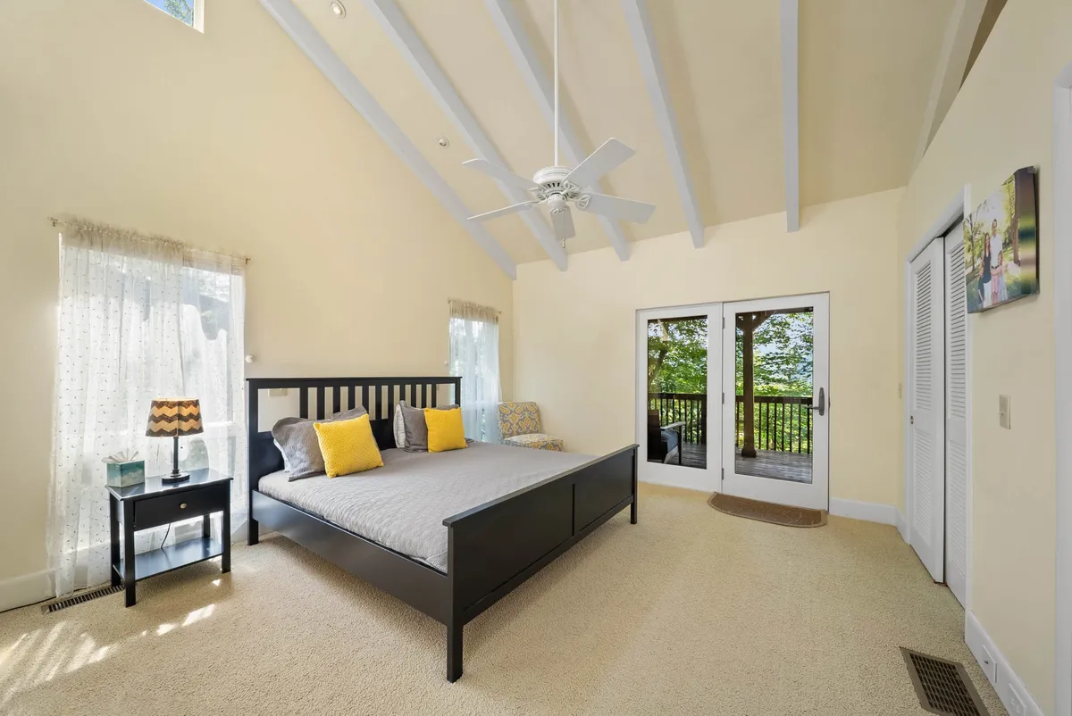 A peaceful bedroom with a plush bed, double doors opening to a balcony, and a nightstand with a softly glowing lamp. The space is filled with natural light and exudes a tranquil, restful atmosphere, inviting guests to step right onto the deck for fresh air and morning sun.