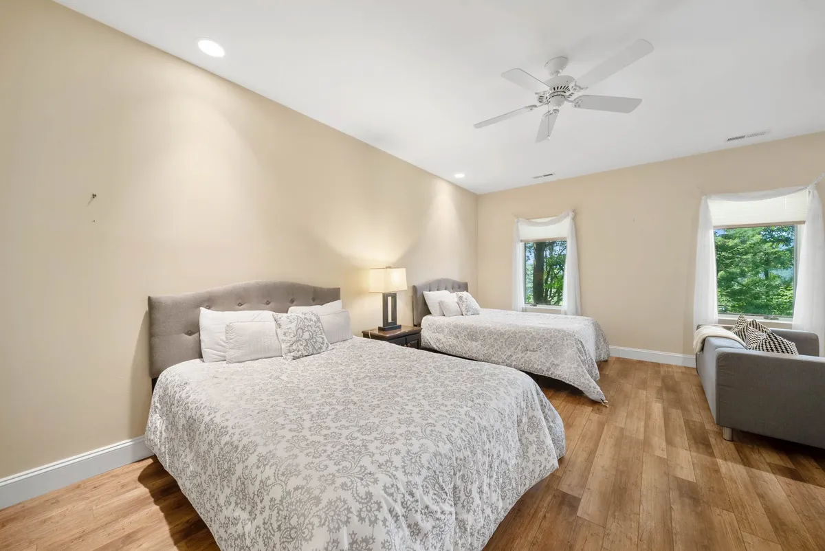 A comfortable interior shot showing two beds, a lamp, and a window seating area. The space is bright with natural light, and the arrangement suggests opportunities for conversation, relaxation, and shared moments among family or friends.