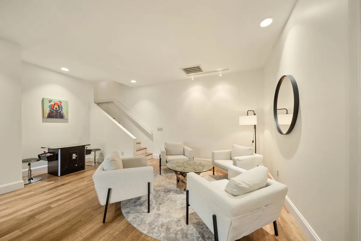 A stylish living area with modern chairs around a round coffee table, complemented by a staircase and artwork on the wall. The natural light and tasteful decor create a serene, contemporary space ideal for casual conversation or sharing highlights from a day out.