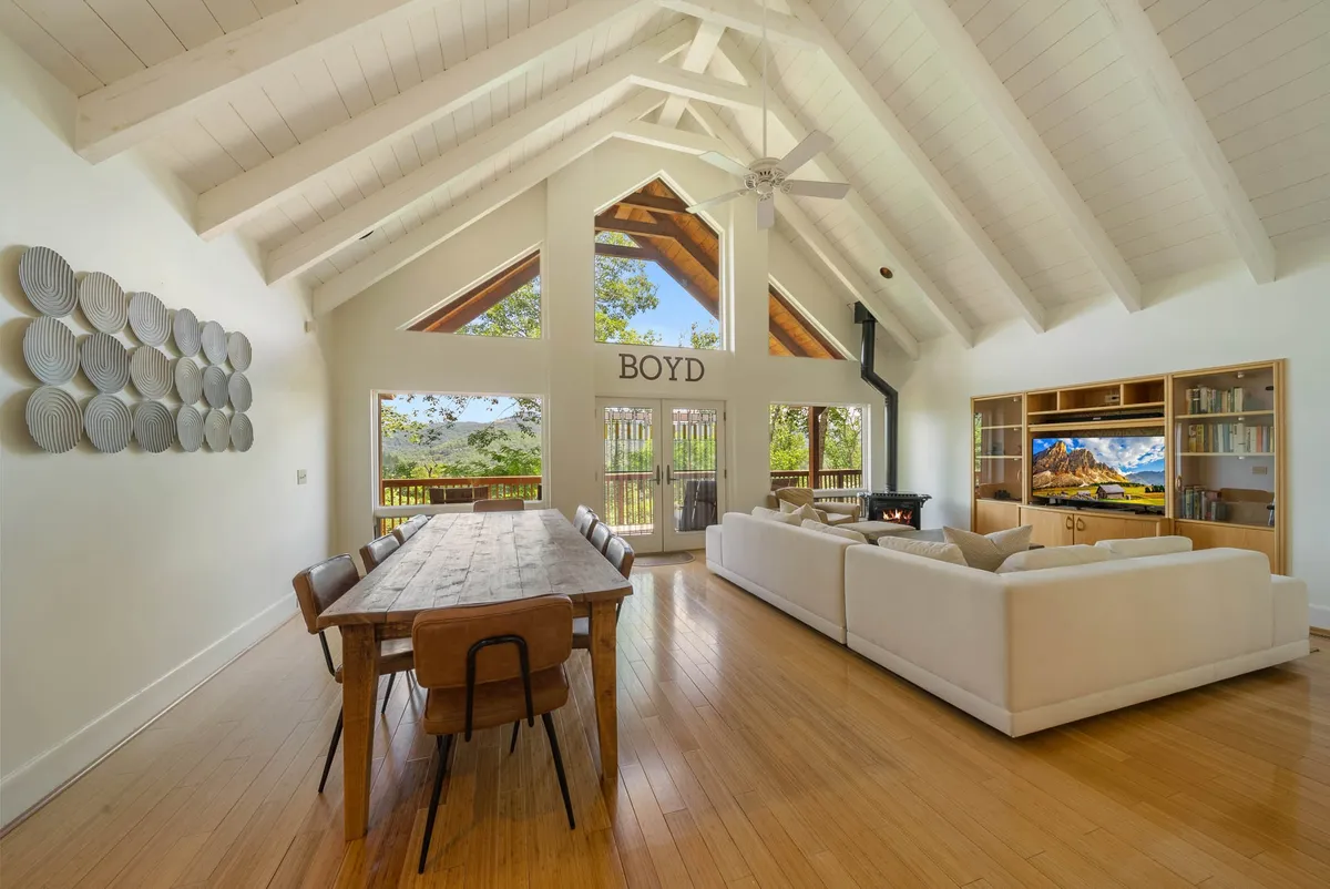 An open-concept living and dining area flooded with natural light from large windows. The space features a comfortable seating area with plush sofas, a dining table ideal for family meals, and decorative wall art. The arrangement encourages gatherings, with plenty of space for games, conversation, or simply soaking up the welcoming and cozy atmosphere.