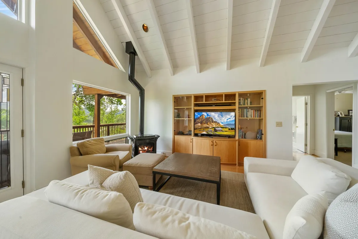 A spacious entertainment room featuring a large sectional sofa, wooden coffee table, TV with a scenic landscape on display, and a cozy wood stove in the corner. The layout encourages group gatherings, with ample seating for both kids and adults. Soft lighting and rustic accents create an inviting, relaxed ambiance.