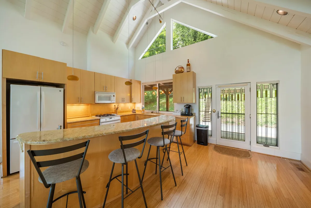 A bright, welcoming kitchen with a central island and bar stools, large windows letting in abundant natural light, and modern appliances. The space is clearly designed for cooking, entertaining, and shared family meals, making it the perfect backdrop for holiday feasts or passing down recipes.