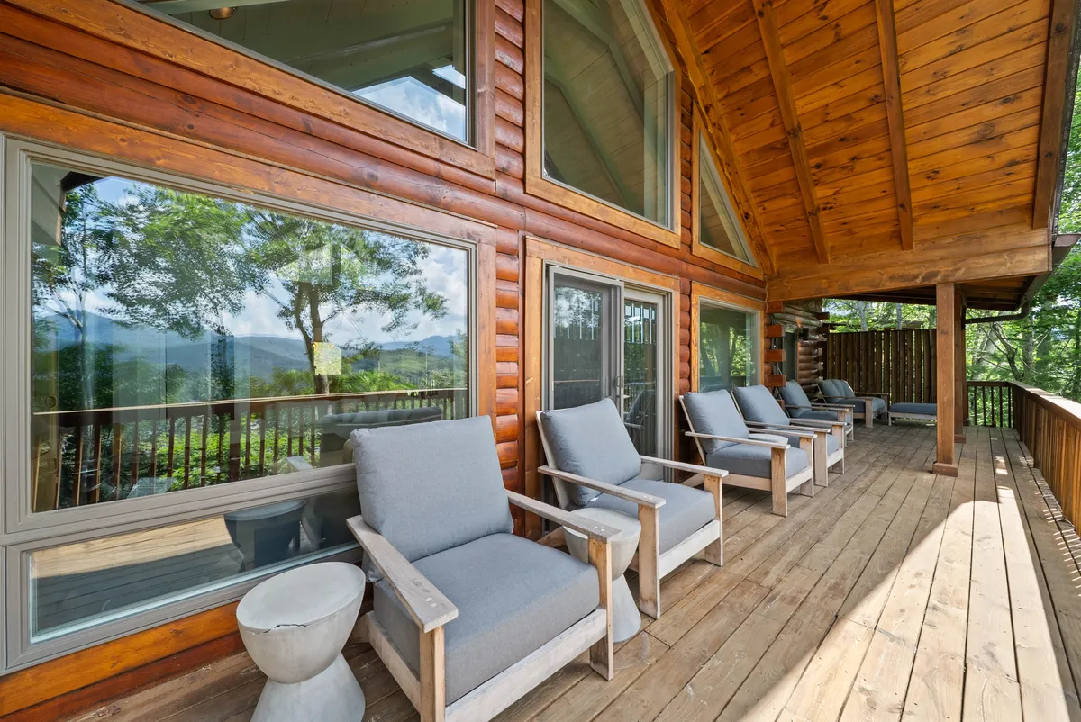 A calm, serene wooden deck with large windows and comfortable seating, set against a backdrop of natural mountain surroundings. The view hints at sunrise or sunset possibilities and invites peaceful moments outdoors at any time of day.