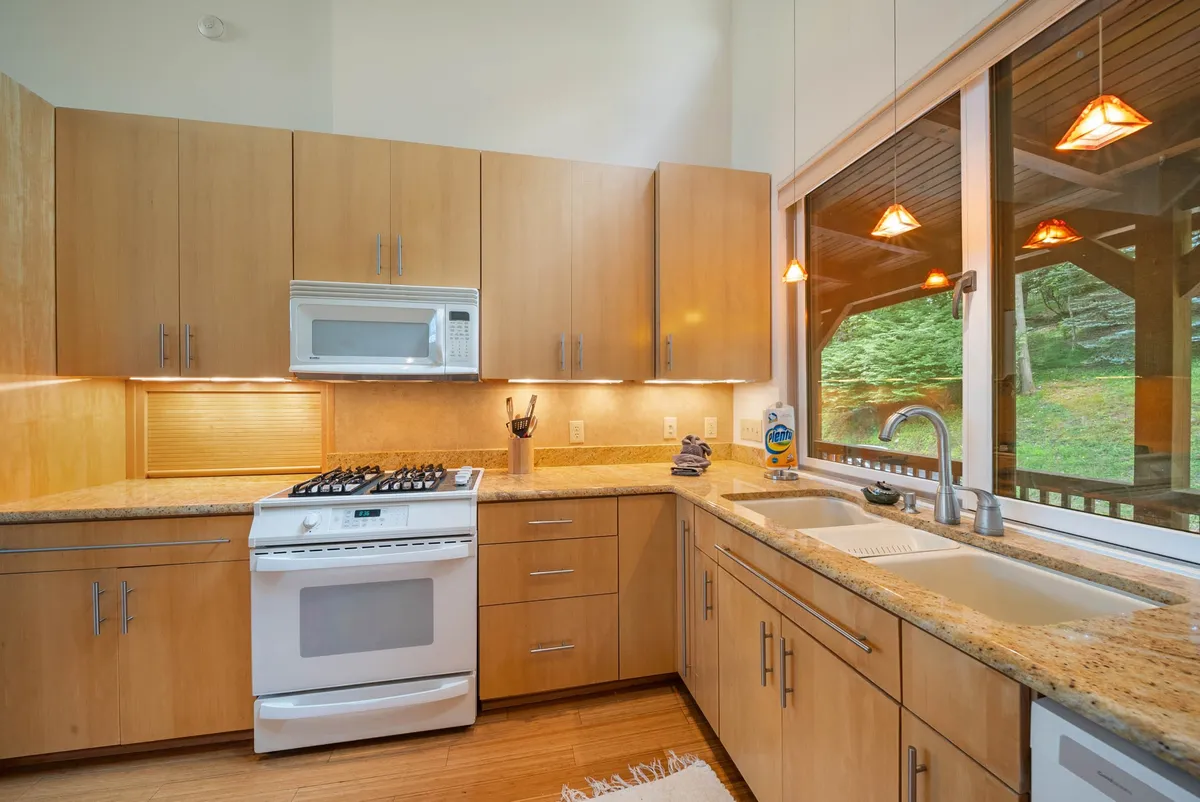 A bright and inviting kitchen with granite countertops, modern appliances, and large windows that showcase the natural landscape outside. Pendant lighting enhances the welcoming atmosphere, making it ideal for family cooking sessions or morning coffee overlooking the scenery.