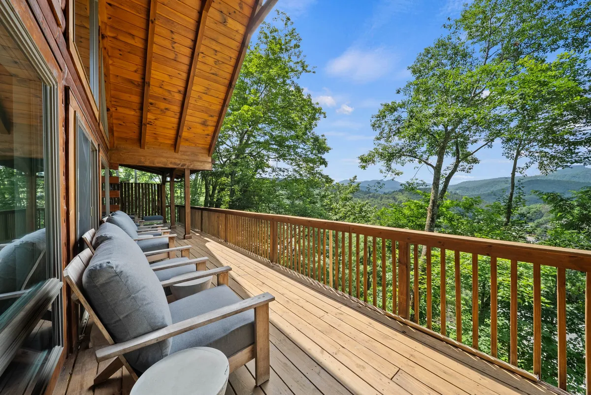 The image captures a spacious wooden wraparound deck outfitted with classic rocking chairs, all overlooking a sweeping mountain view framed by lush green foliage. The atmosphere is peaceful and inviting, ideal for relaxing, reading, or socializing while immersed in the natural surroundings.