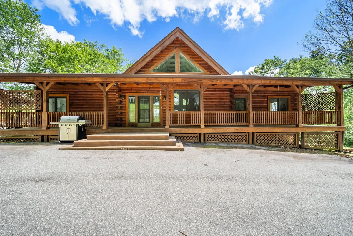 Displaying the classic log cabin structure with a wide front porch, large windows, and attractive landscaping, this image conveys warmth and a touch of rustic charm. The porch provides a gathering spot to enjoy the scenery, emphasizing the home as both a starting point for adventures and a cozy place to return to.