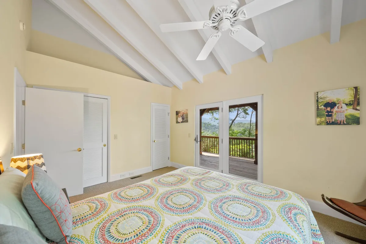 A tranquil bedroom featuring a bed with a colorful quilt, large windows that frame the view, and artwork on the wall. The natural light invites cozy mornings or peaceful moments spent admiring sunsets from inside the cabin.